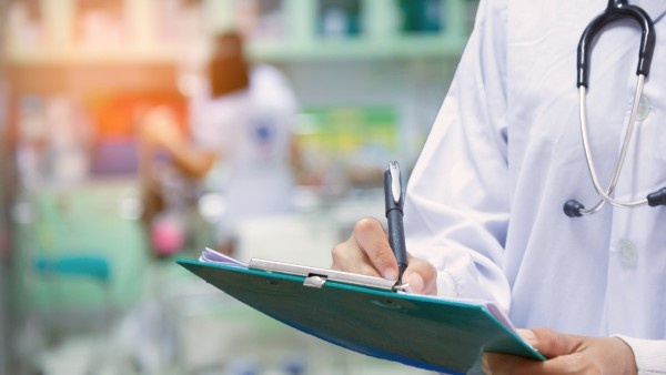 Doctor wearing a white coat filling out a medical chart