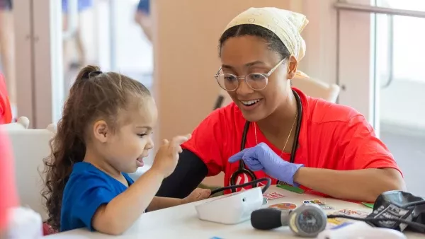 A health care provider sits next to a child demonstrating a medical instrument