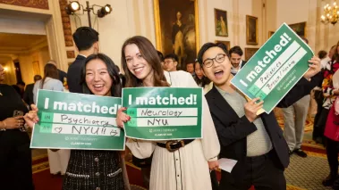 Three people standing in a formal indoor space, holding signs that say I Matched!